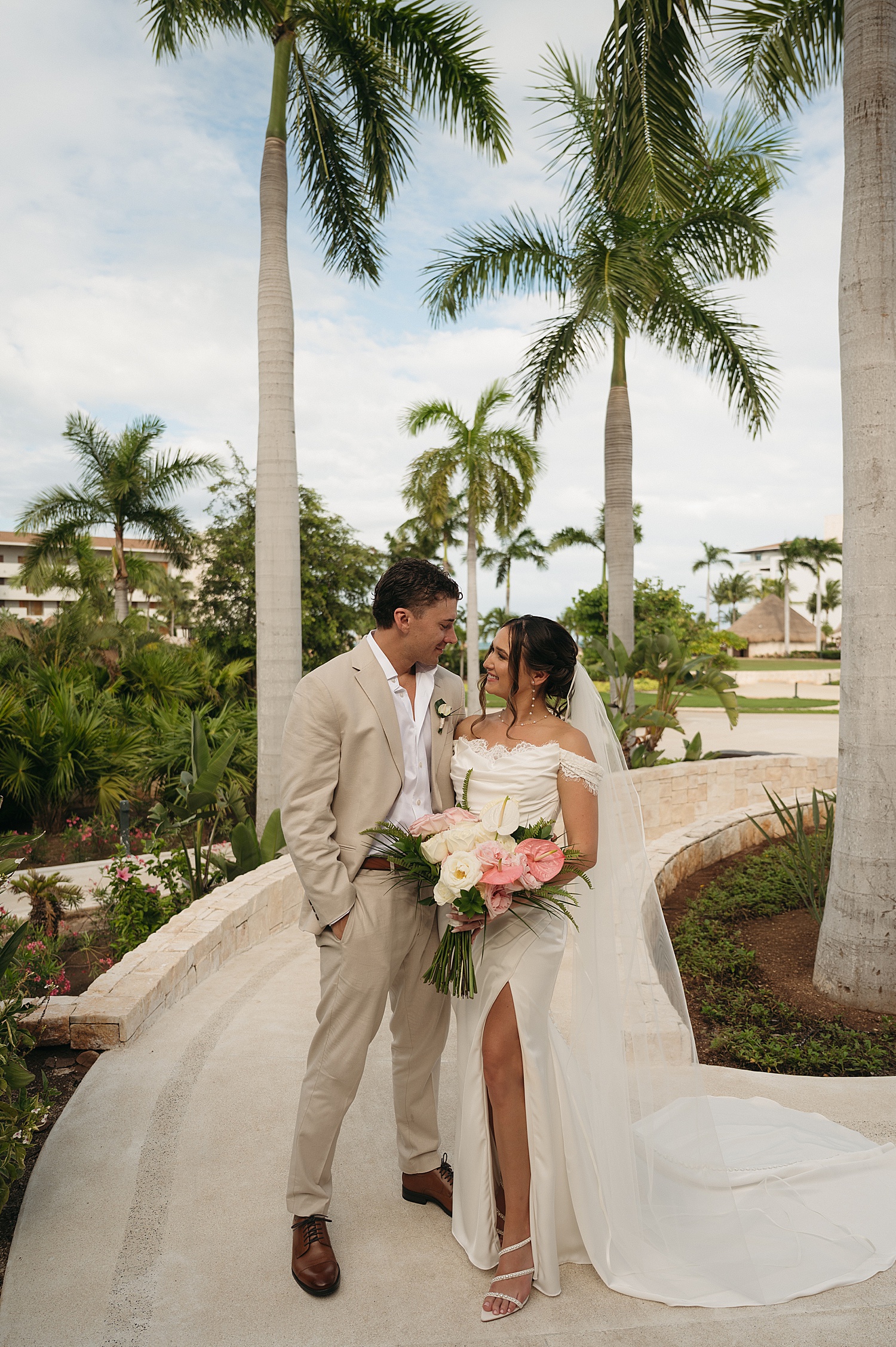 couple stand under big palm trees on a sidewalk at Dreams Playa Mujeres