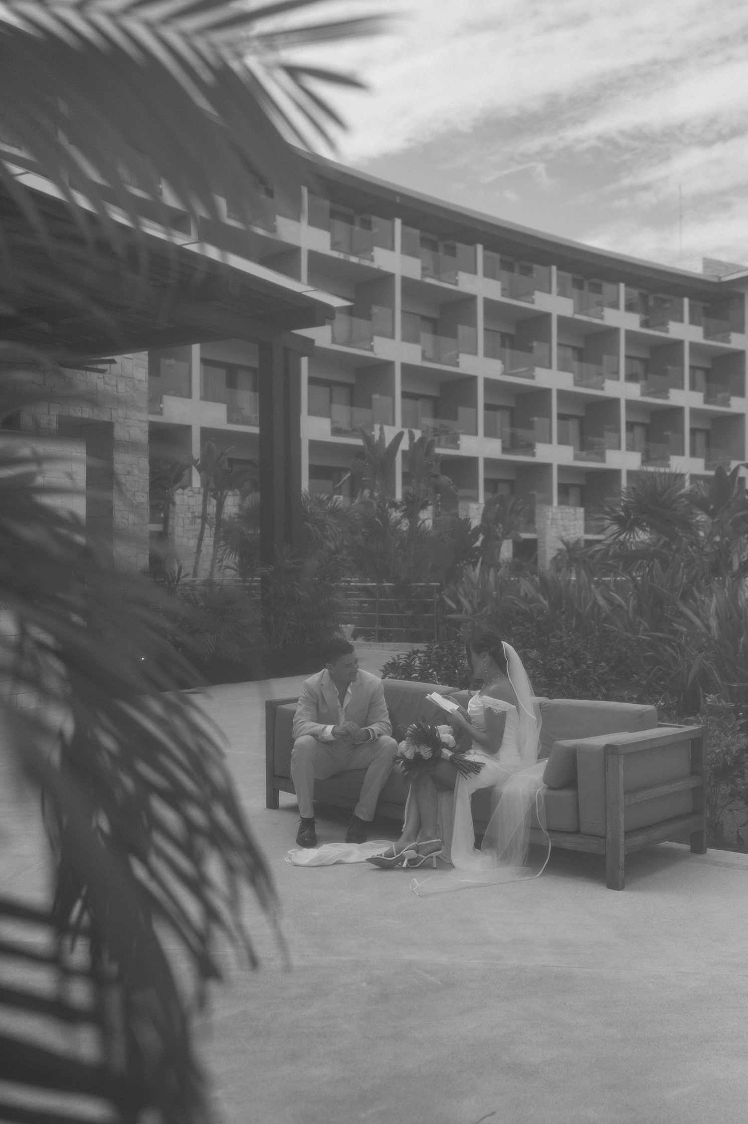 bride and groom sit on private couch under palm trees at resort by Travel Elopement Photographer