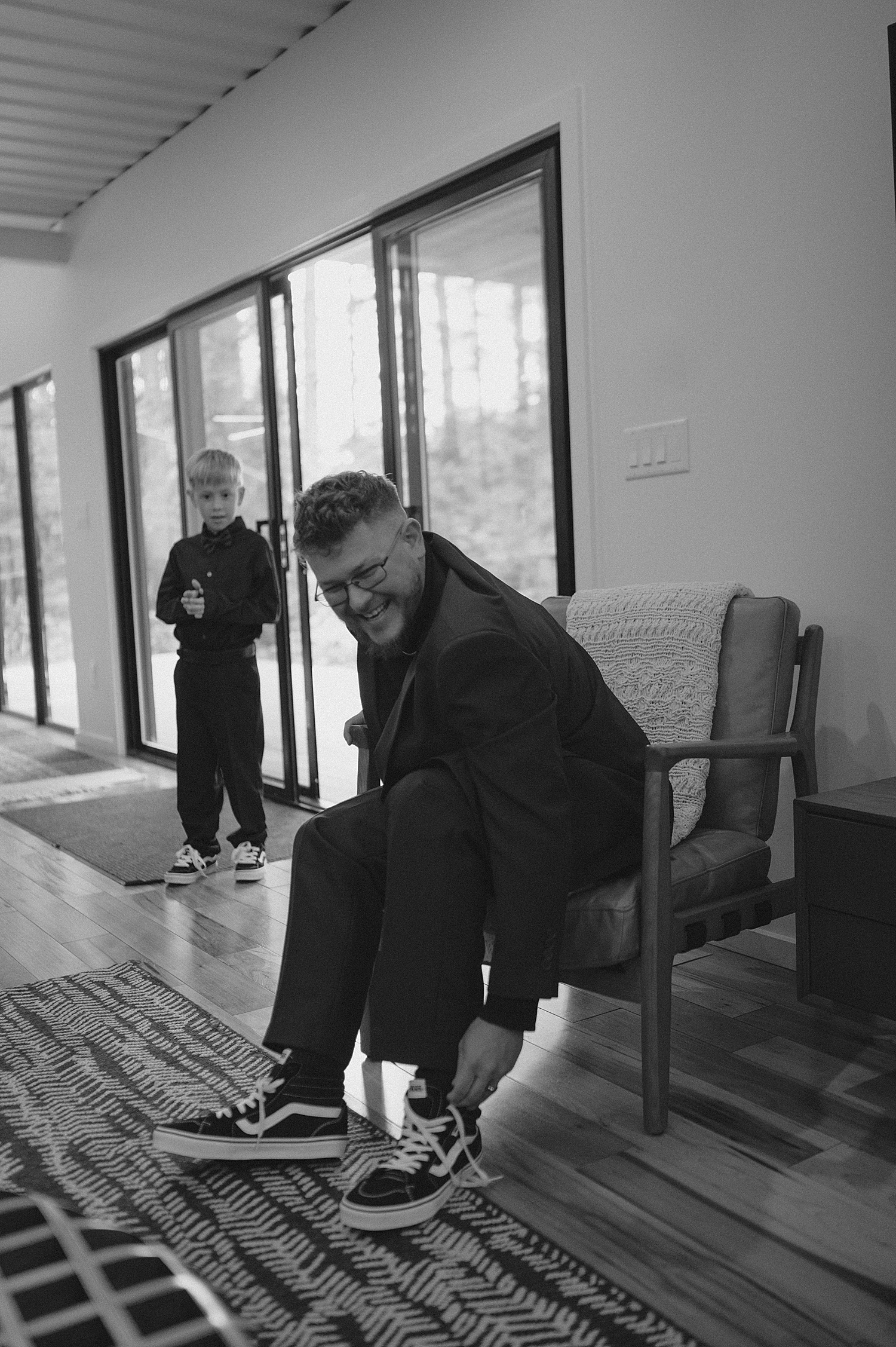 dad puts on his shoes next to sliding glass doors by Thistle and Veil Photography