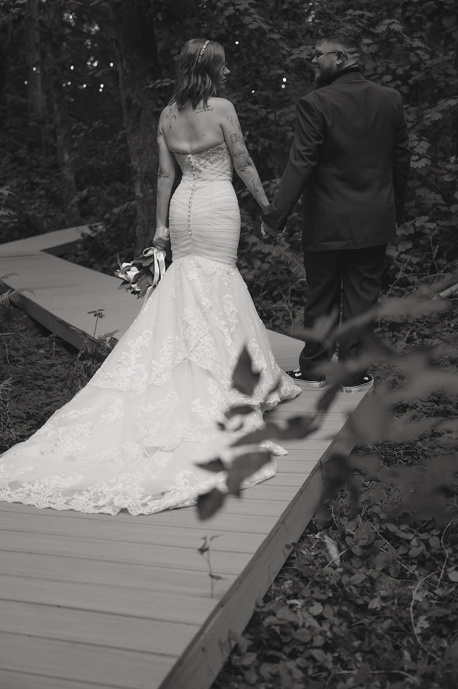 bride and groom walk down wooden path in trees for vow renewal