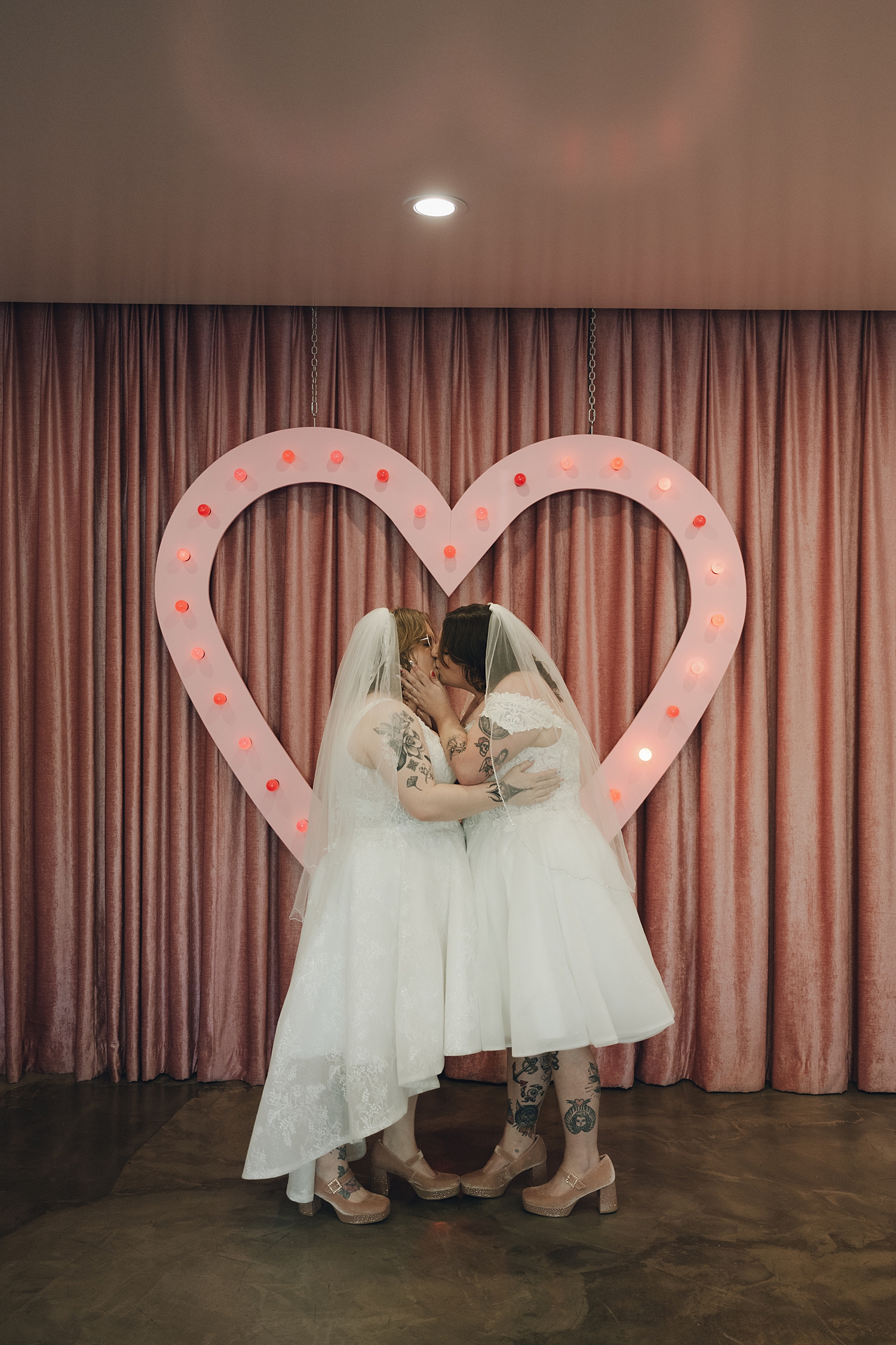 newlyweds share a kiss in front of neon pink heart by Thistle and Veil Photo
