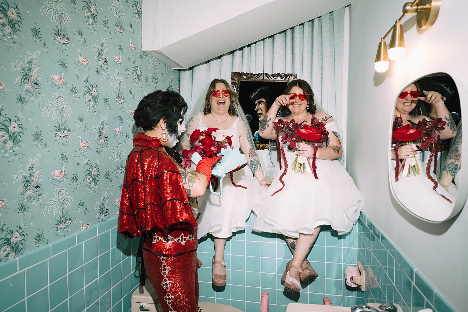 couple sits on blue bathroom counter next to devilish Elvis at Sure Thing Chapel