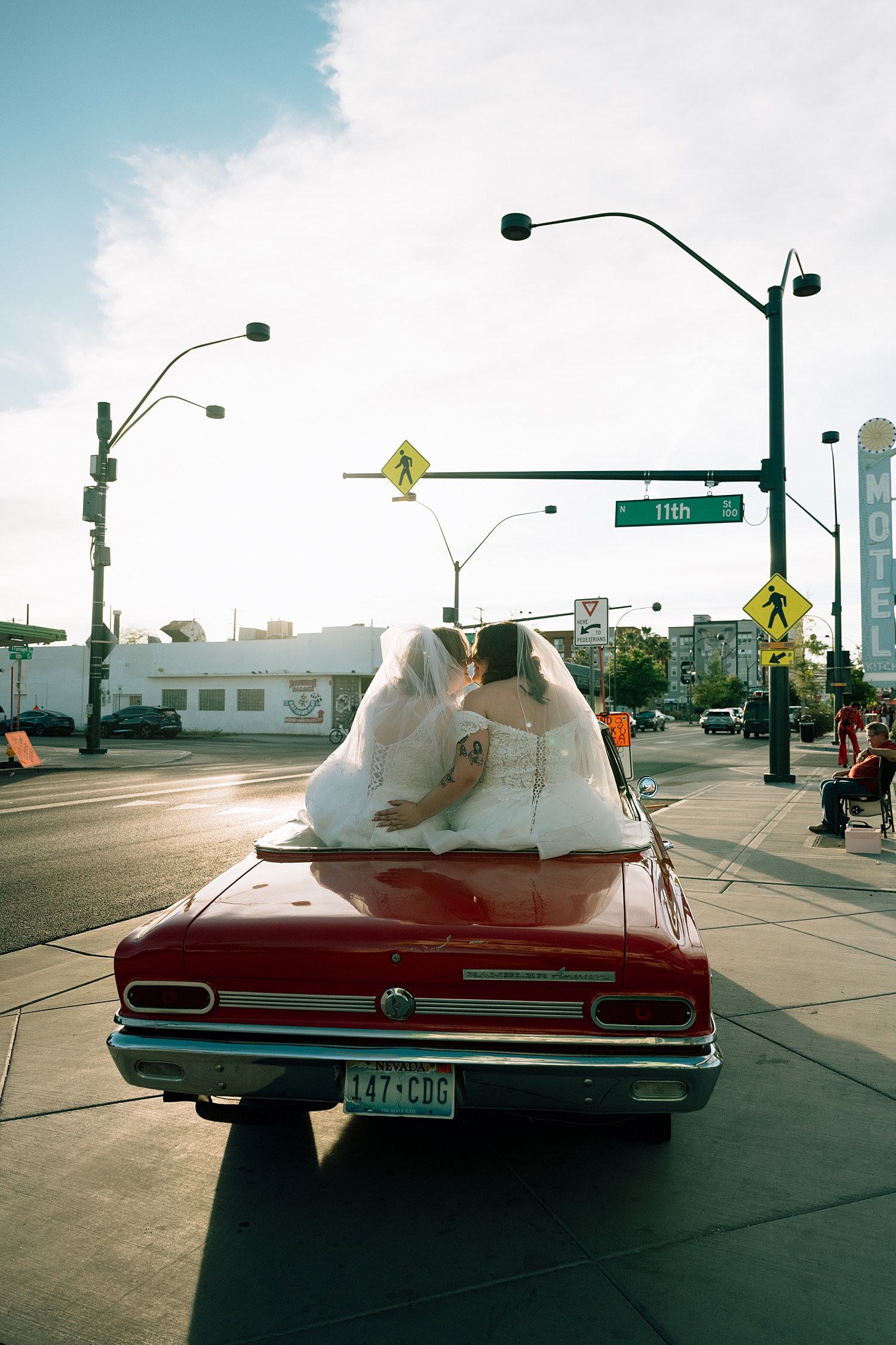 newlyweds sitting on vintage red car on street outside Sure Thing Chapel