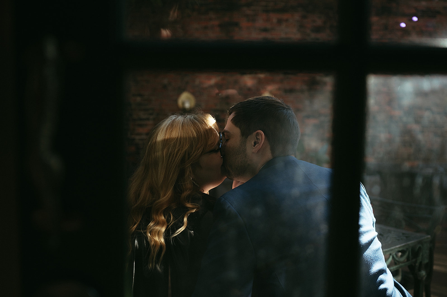 engaged couple kiss behind coffee shop window for non-traditional engagement photos